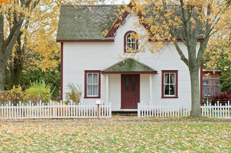 A white clapboard house with a red door under autumn maple trees
